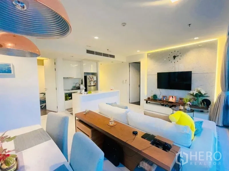 Condominium for rent or sale in Sathon, Bangkok - Open-plan living area with TV feature wall, sofa and white kitchen island.