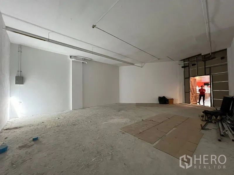 Retail Space for rent - Open-plan retail shell with white walls, concrete floor, overhead strip lighting and a wide front opening, ready for fit-out in Watthana.