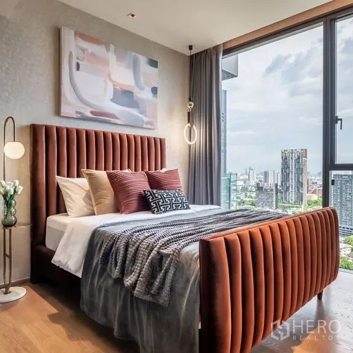 Condominium for rent in Khlong Toei, Bangkok - Second bedroom featuring a rust-colored upholstered bed, contemporary art and wide city views.