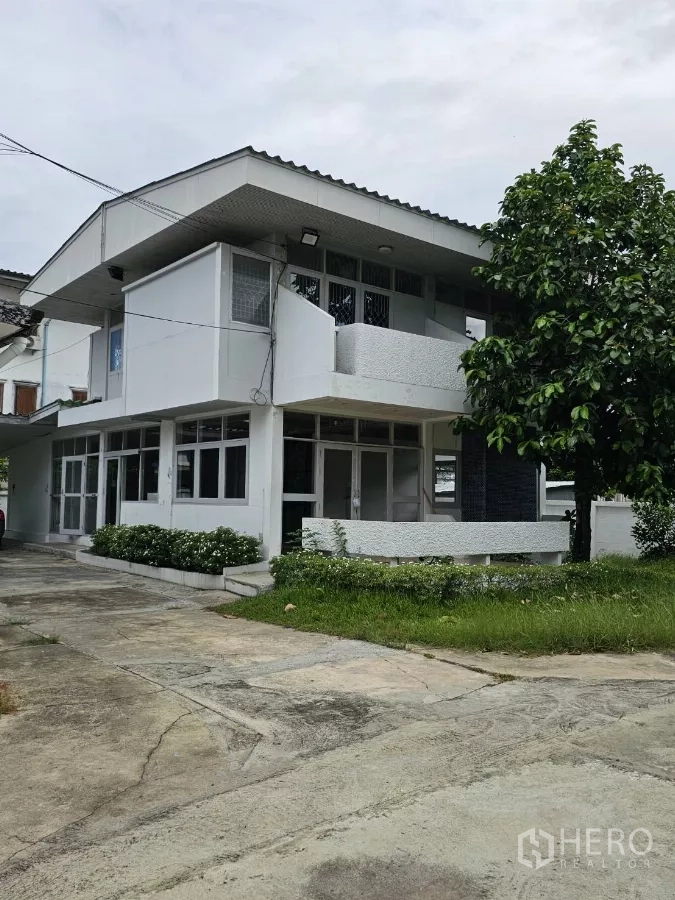Detached House for rent or sale in Lat Phrao, Bangkok - Corner angle showing balcony, glazed doors, and grass beside the driveway.