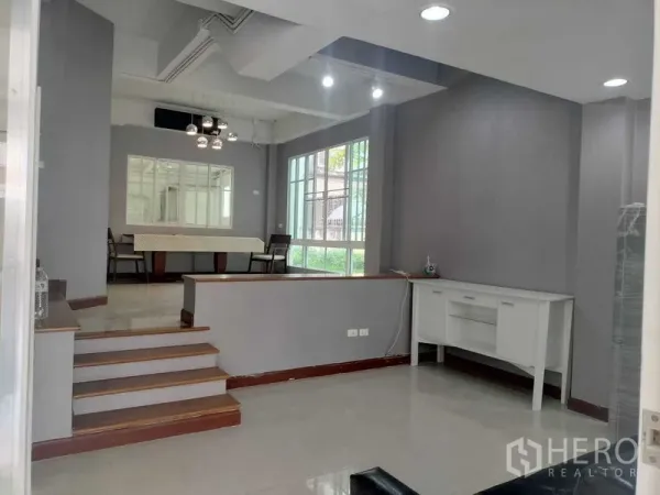 Townhouse for rent in Bueng Kum, Bangkok - Open-plan dining and lounge area with steps, large windows and grey walls.