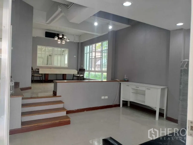Townhouse for rent in Bueng Kum, Bangkok - Open-plan dining and lounge area with steps, large windows and grey walls.