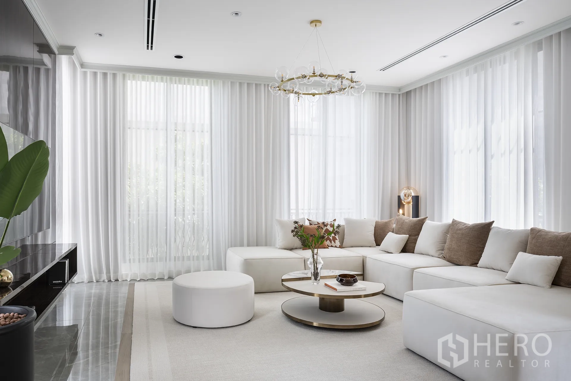 Detached House for sale in Yan Nawa, Bangkok - Bright living room with a large white sectional sofa, round coffee table, modern chandelier and floor-to-ceiling curtains.