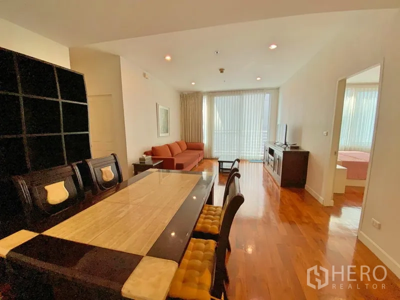 Condominium for rent in Khlong Toei, Bangkok - Dining area with marble-top table and seating, opening to a light-filled lounge.