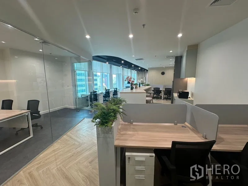 Office Space for rent - Open office cubicle with wood desk, drawers and glass-walled room nearby.