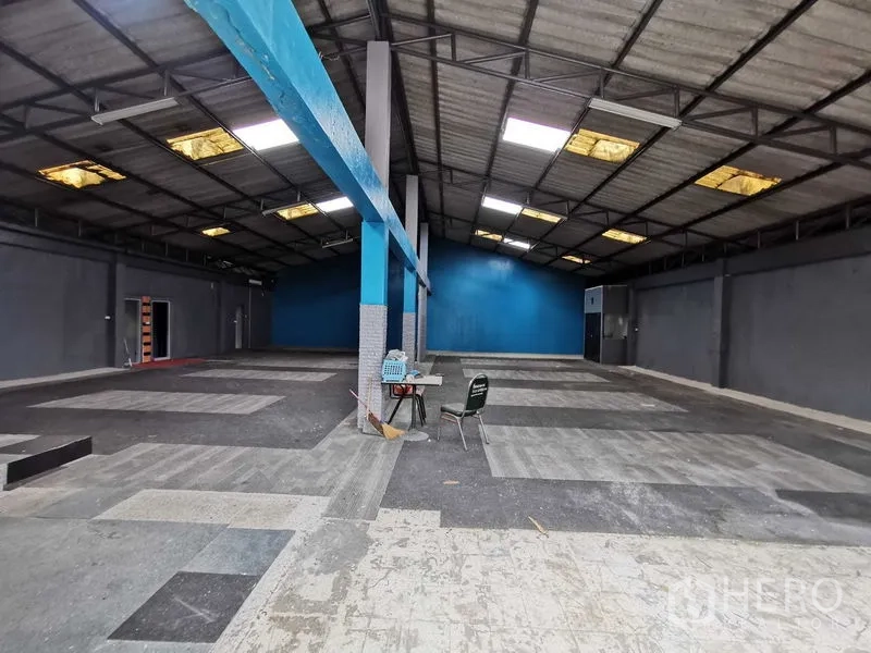Warehouse for rent in Nonthaburi - Wide warehouse bay featuring central support columns, a blue feature wall and mixed tile flooring.