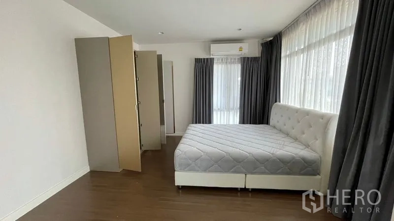 Detached House for rent in Bang Kapi, Bangkok - Master bedroom with large bed, corner glass windows, curtains and wardrobes.