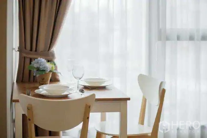 Condominium for rent in Khlong Toei, Bangkok - Small dining table for two beside sheer-curtained window with natural light.