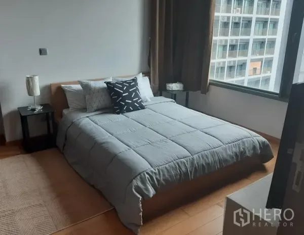 Condominium for rent in Khlong Toei, Bangkok - Cozy bedroom with double bed, bedside tables, wood flooring and a large window facing nearby buildings.