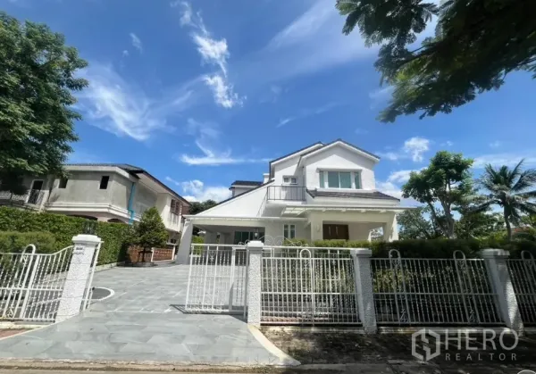 บ้าน ให้เช่าในMueang Samut Prakan, Samut Prakan - มุมหน้าบ้านเดี่ยวสีขาวสองชั้น รีโนเวทใหม่ พร้อมรั้วและทางรถเข้าภายใต้ท้องฟ้าใส