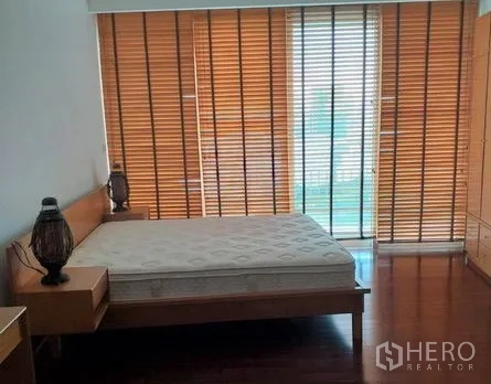Condominium for rent in Pathum Wan, Bangkok - Primary bedroom with wooden floors, queen bed, and large window fitted with timber blinds.
