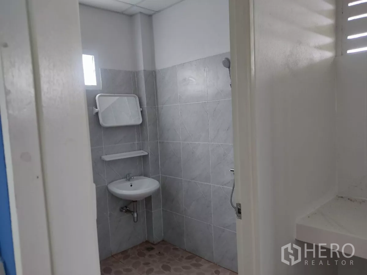 Factory for sale in Khlong Toei, Bangkok - Clean tiled restroom with sink, mirror and handheld shower.