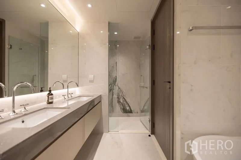 Condominium for rent in Pathum Wan, Bangkok - Luxury bathroom with double vanity, large mirror and marble-lined shower.
