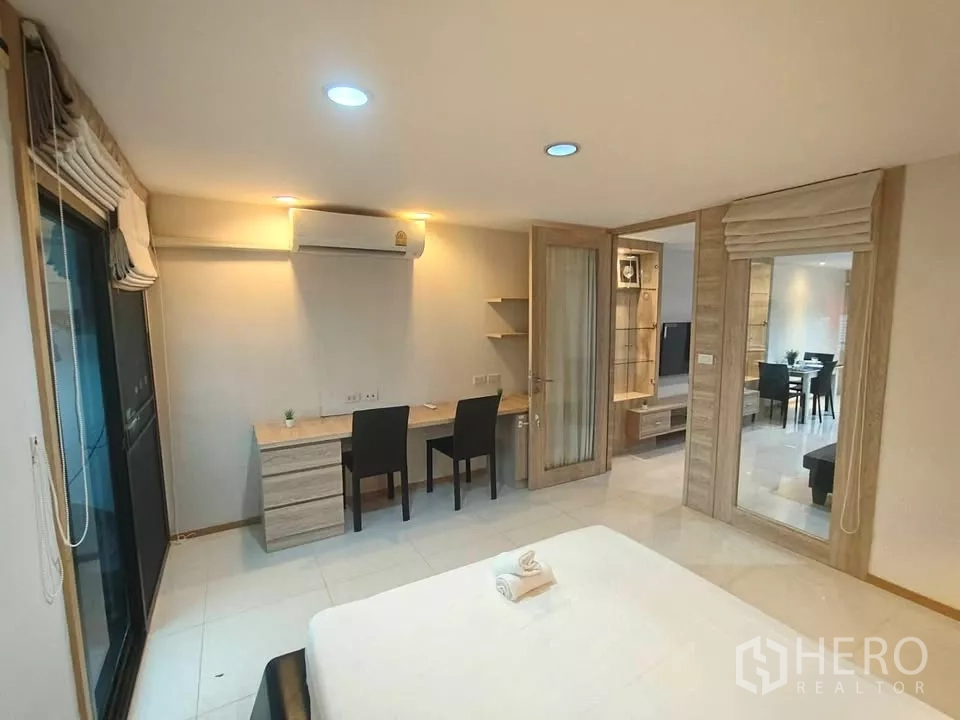 Condominium for rent in Khlong Toei, Bangkok - Primary bedroom with a study desk for two, air conditioning, and sliding door access to a balcony.