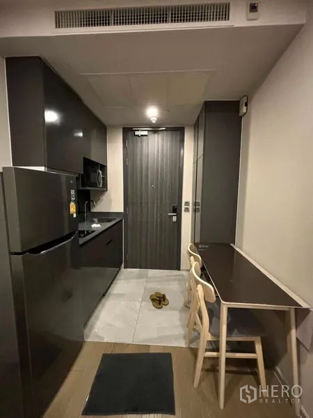 Condominium for rent in Watthana, Bangkok - Compact kitchenette with glossy cabinets, refrigerator, microwave and a small dining nook.