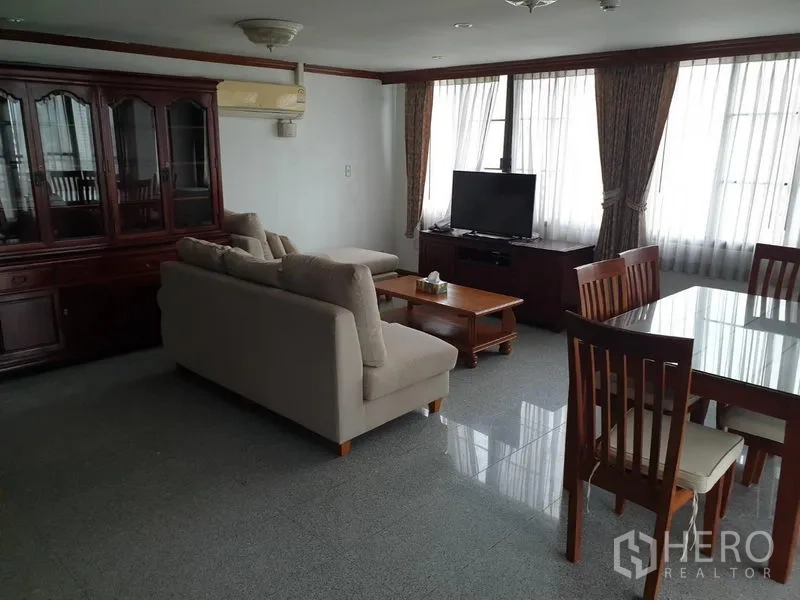 公寓 出租在Watthana, Bangkok - 开放式客餐厅，米色沙发、电视柜、木质餐桌椅与大面积落窗。