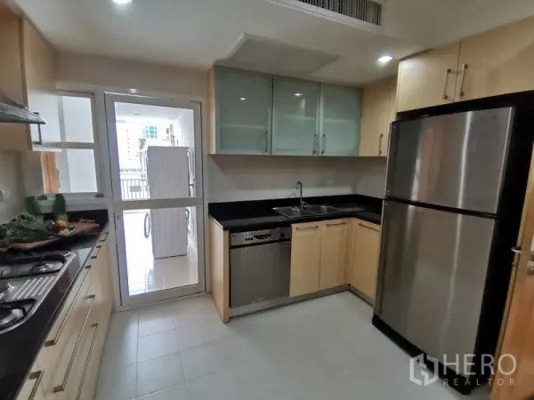 Condominium for rent in Khlong Toei, Bangkok - Modern closed kitchen with black countertops, stainless refrigerator, dishwasher, glass-front cabinets, and door to a utility area.