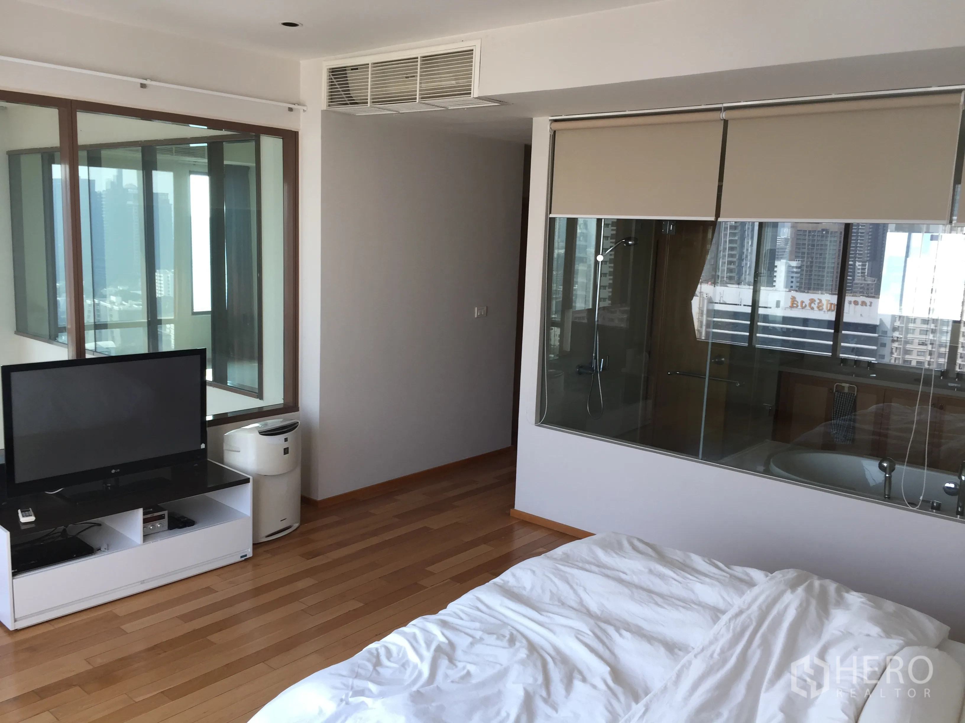 Condominium for rent or sale in Khlong Toei, Bangkok - Master bedroom with TV console, hardwood floors and glass wall to ensuite bathroom with city views.