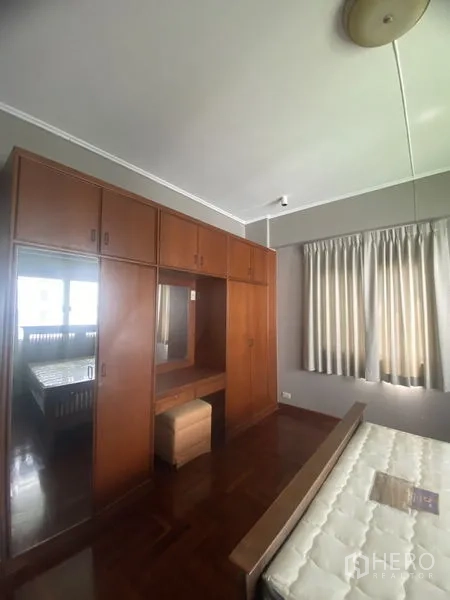 公寓 出租在Sathon, Bangkok - 卧室带大型木质嵌入式衣柜与梳妆台，窗帘与木地板。