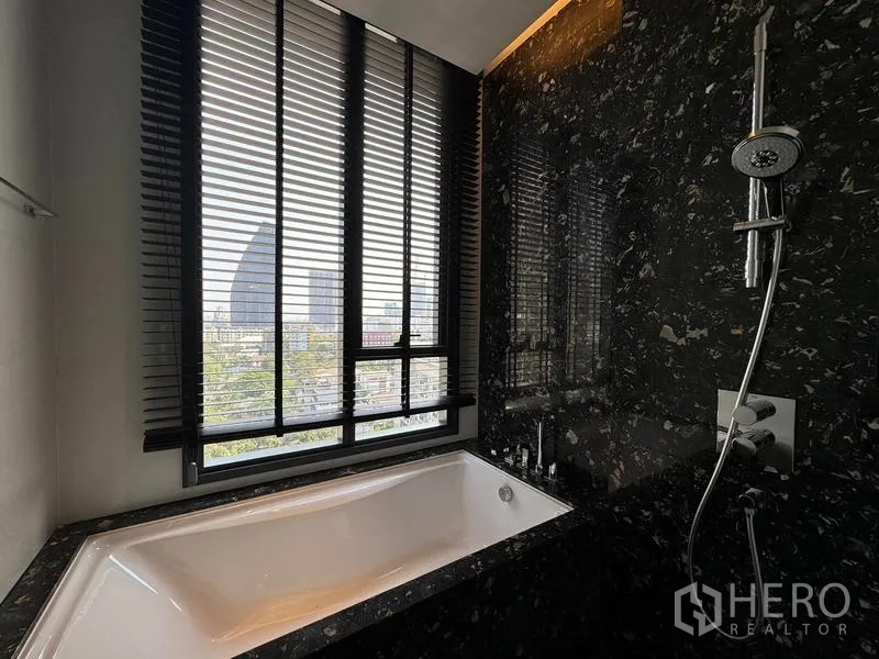 Condominium for rent - Bathtub by large window with blinds and separate handheld shower on marble wall.