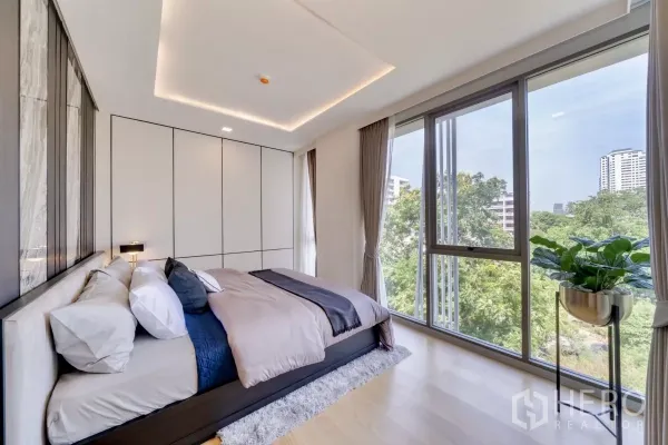公寓 出租在Watthana, Bangkok - 主卧配转角落地窗，俯瞰绿意与城市景观，木地板温暖。