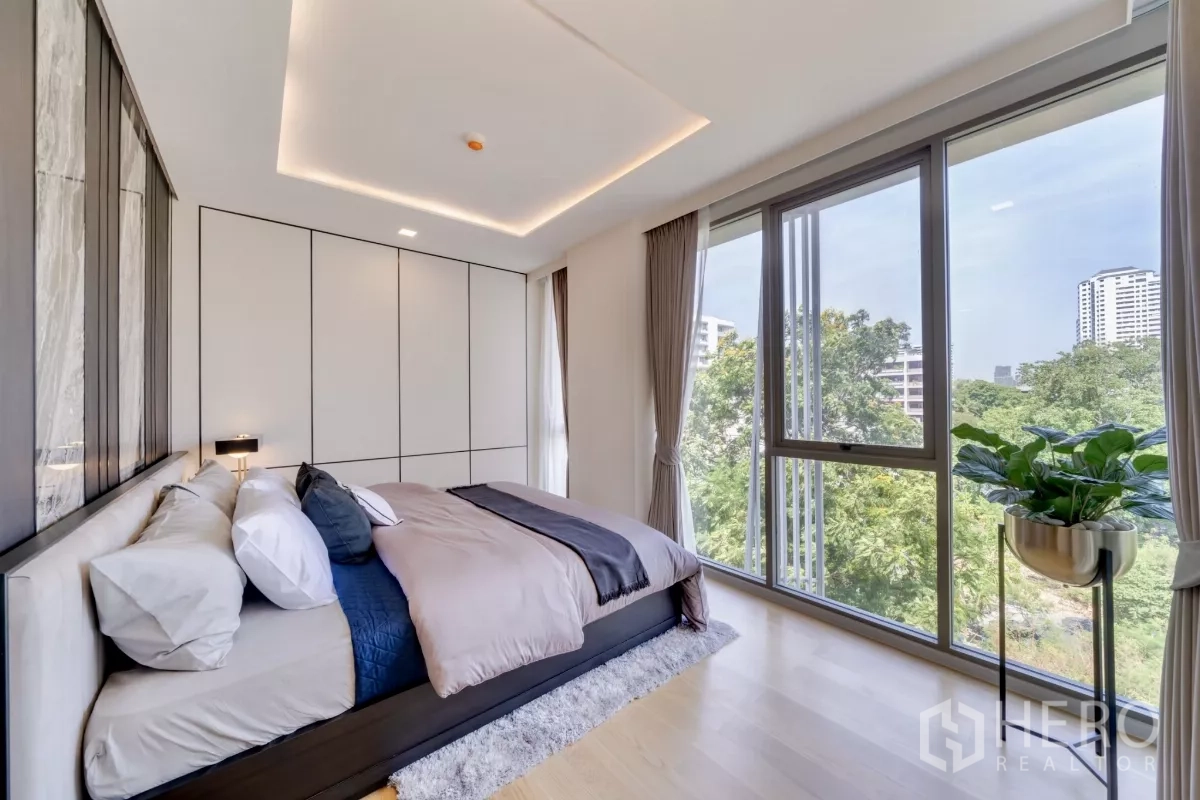 公寓 出租在Watthana, Bangkok - 主卧配转角落地窗，俯瞰绿意与城市景观，木地板温暖。
