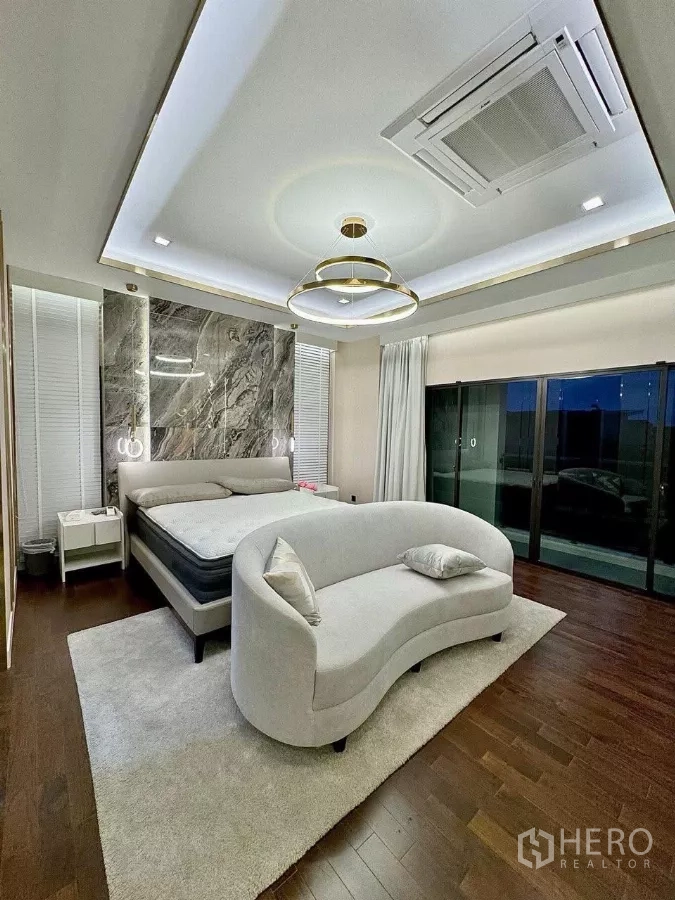 Detached House for sale in Saphan Sung, Bangkok - Elegant bedroom with stone headboard feature, curved sofa and recessed ceiling lighting.