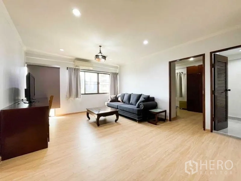 Condominium for rent or sale in Khlong Toei, Bangkok - Spacious living room with sofa, TV cabinet and doors to the bedrooms.