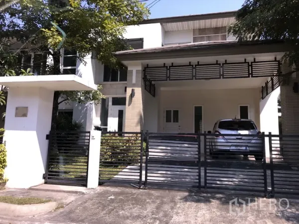 Detached House for sale in Saphan Sung, Bangkok - Two-storey detached house in Saphan Sung, Bangkok with gated driveway, covered two-car carport and an upper balcony shaded by trees.