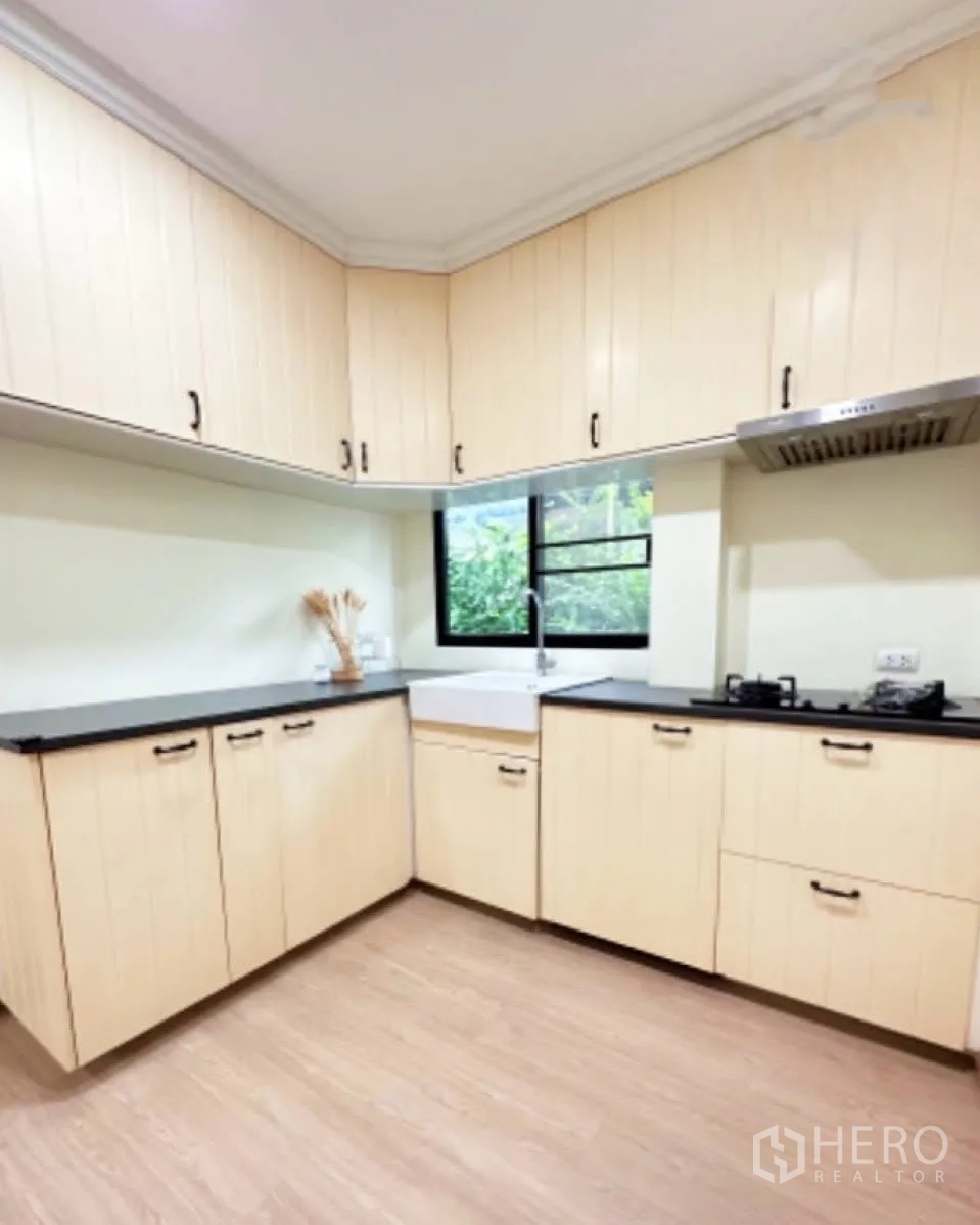 Detached House for sale in Lam Luk Ka, Pathum Thani - U-shaped kitchen fitted with light wood cabinets, black countertops, gas hob and a window.