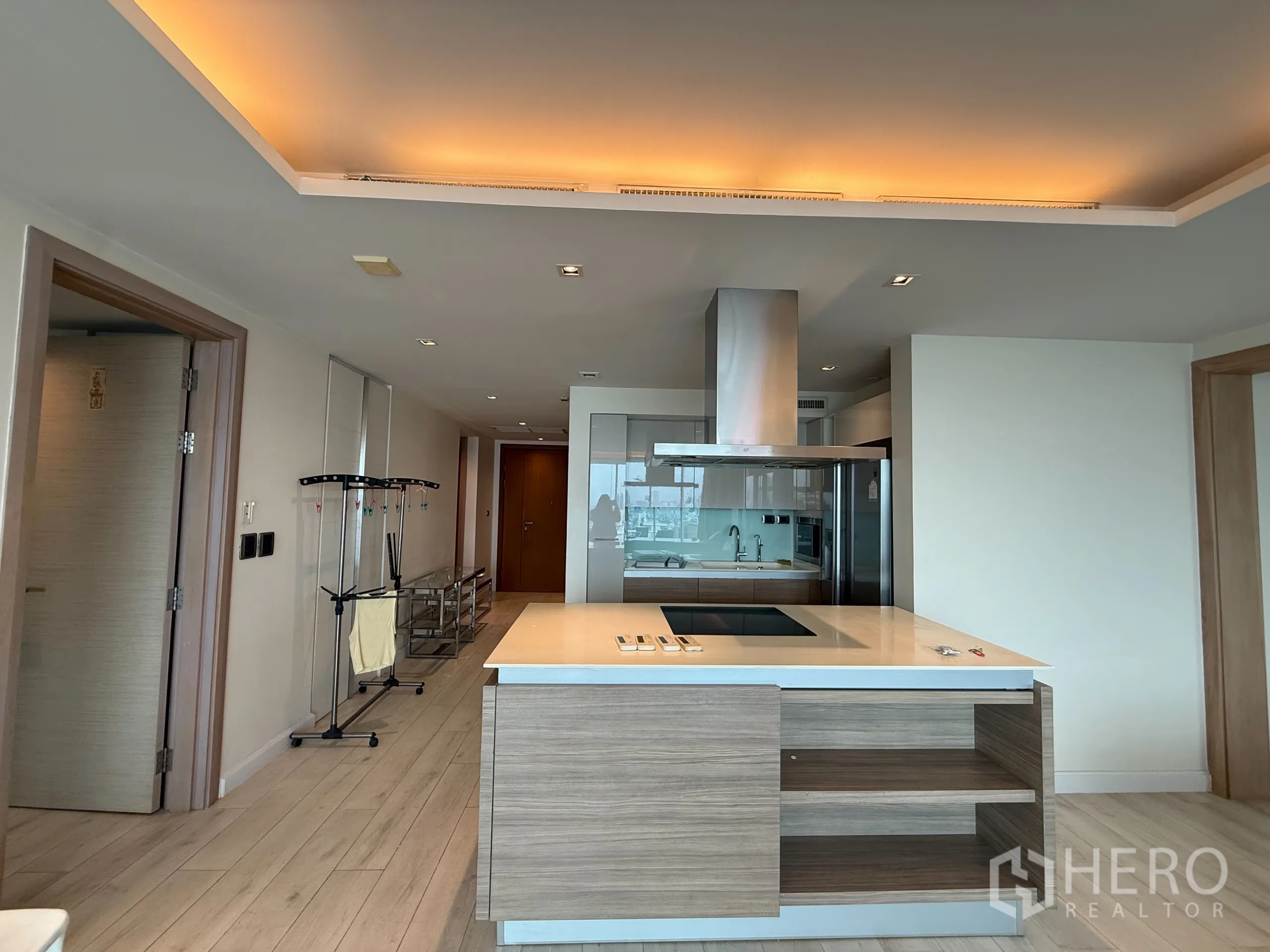 Condominium for rent in Phaya Thai, Bangkok - Modern kitchen island with hob and stainless hood, light wood cabinetry and corridor beyond.