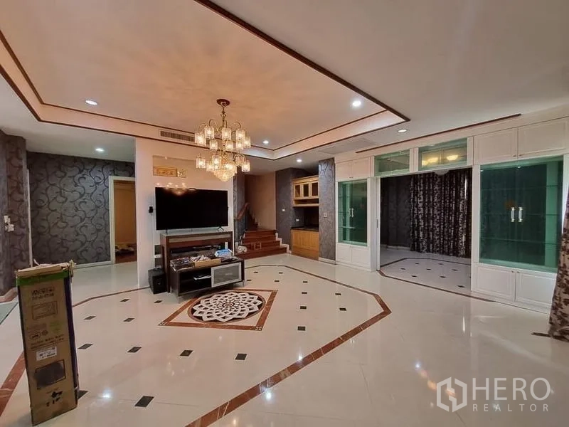 Detached House for rent in Yan Nawa, Bangkok - Spacious living room with chandelier ceiling, polished tile floors, TV wall and staircase.