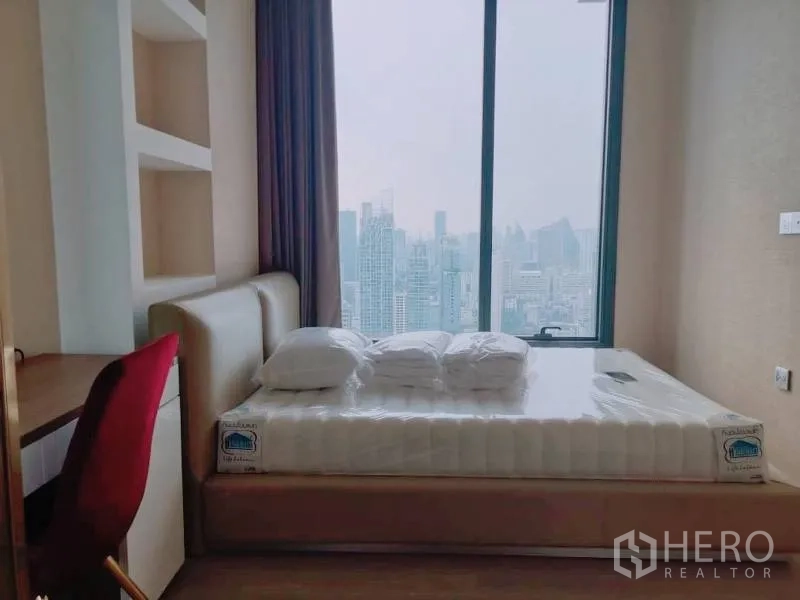 Condominium for rent or sale in Watthana, Bangkok - Bedroom with large window and skyline view, built-in shelving and study desk.