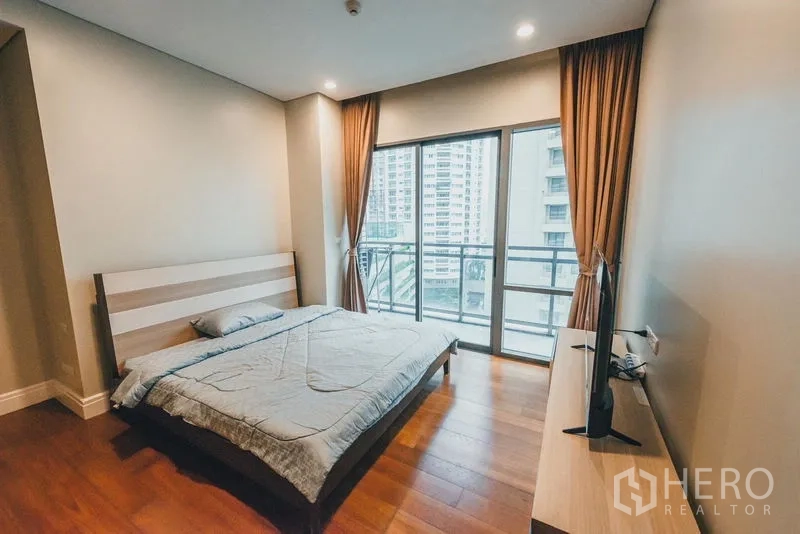 Condominium for rent in Khlong Toei, Bangkok - Master bedroom with balcony access, large windows, curtains and wood flooring.