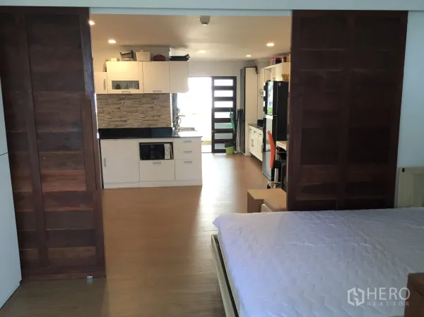 Condominium for rent in Watthana, Bangkok - Open-plan studio layout with bed and kitchen separated by wooden sliding doors.