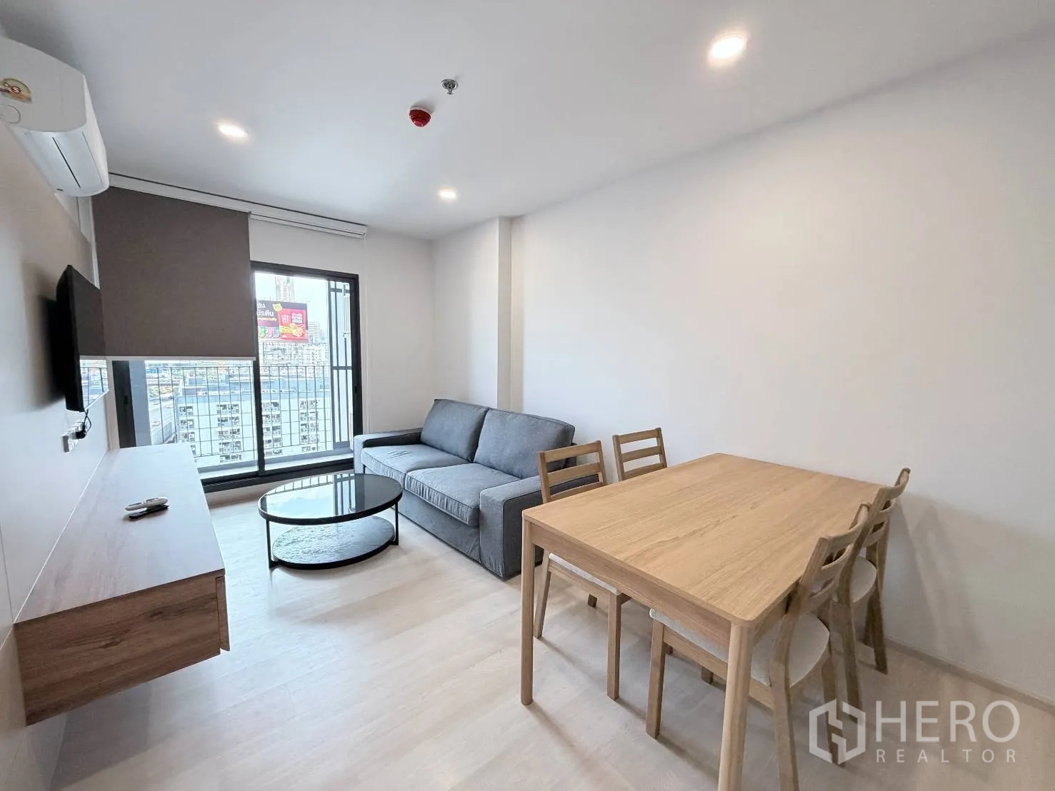 公寓 for rent in Din Daeng, Bangkok - 客餐厅设灰色沙发、圆形茶几、木质餐桌椅及通往阳台的玻璃门。