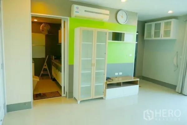 Condominium for rent or sale in Khlong San, Bangkok - Bright living area with green accent wall, glass display cabinet and air conditioning.