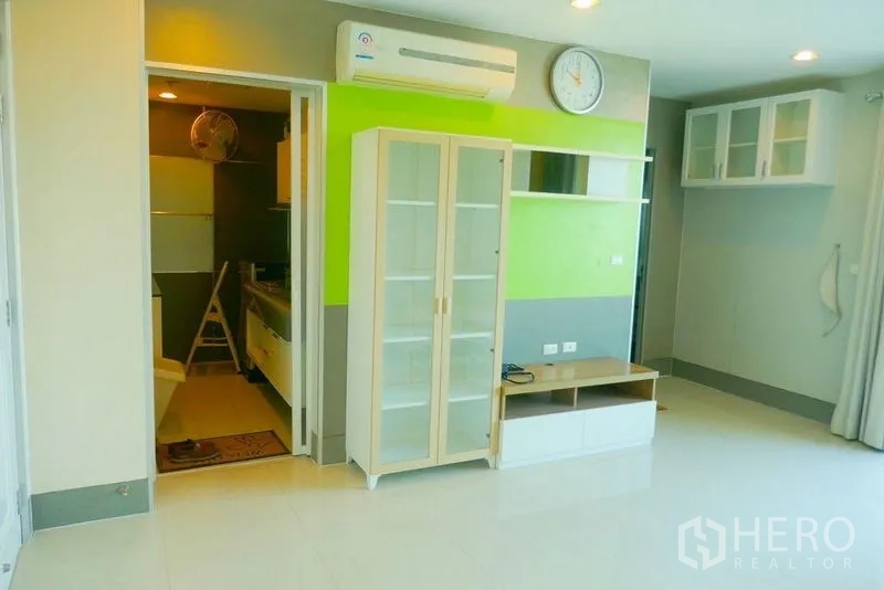 Condominium for rent or sale in Khlong San, Bangkok - Bright living area with green accent wall, glass display cabinet and air conditioning.