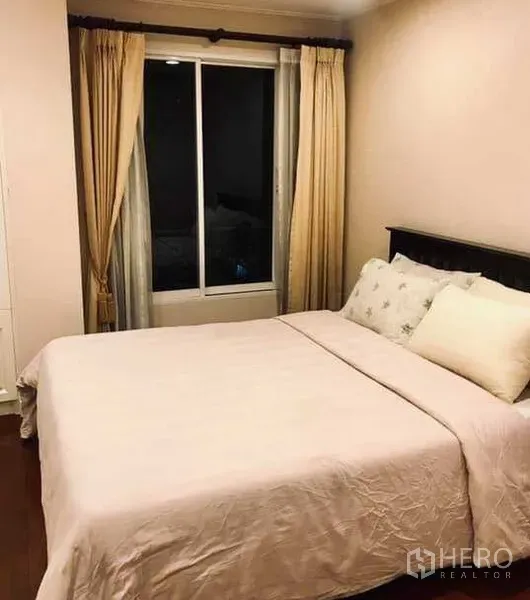 Condominium for rent in Khlong Toei, Bangkok - Cozy second bedroom with window, cream curtains and warm lighting.