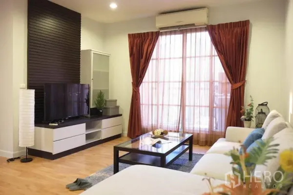 公寓 出租在Khlong Toei, Bangkok - 明亮客厅，L型沙发、电视柜、木地板与带窗帘的推拉落地门。