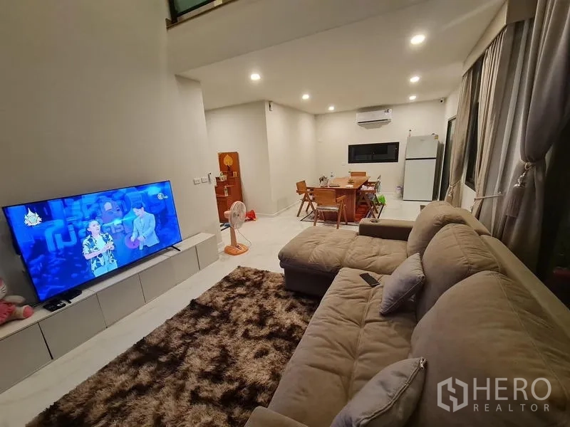 Detached House for rent in Bang Bo, Samut Prakan - Bright living and dining area with L-shaped sofa, TV wall and recessed lights.