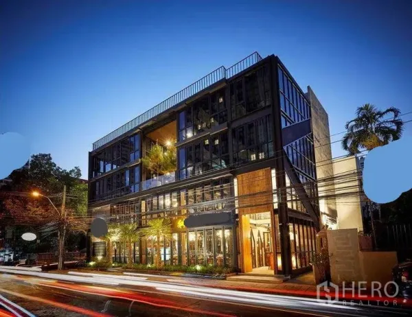 Retail Space for rent in Watthana, Bangkok - Contemporary glass-fronted commercial building at dusk with lit retail frontage and landscaping.