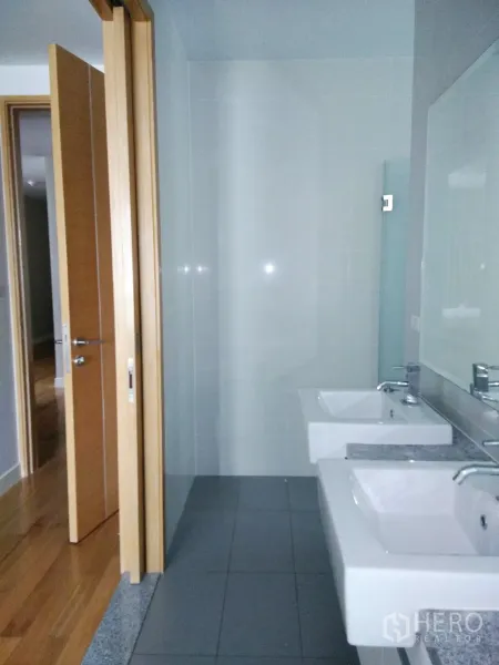 Condominium for rent in Khlong Toei, Bangkok - Contemporary bathroom with double sinks, large mirror, and glass shower.