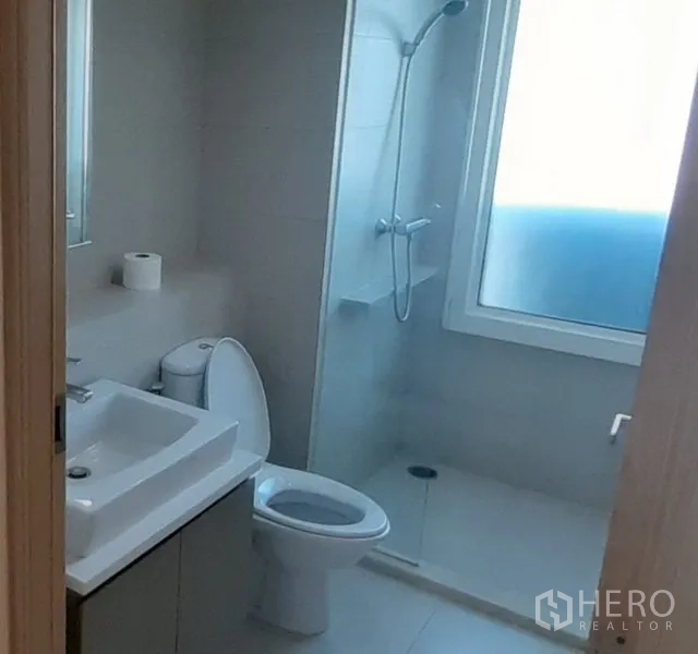 Condominium for rent in Khlong Toei, Bangkok - Bathroom with windowed shower, square-basin vanity, and ceramic toilet in light tones.