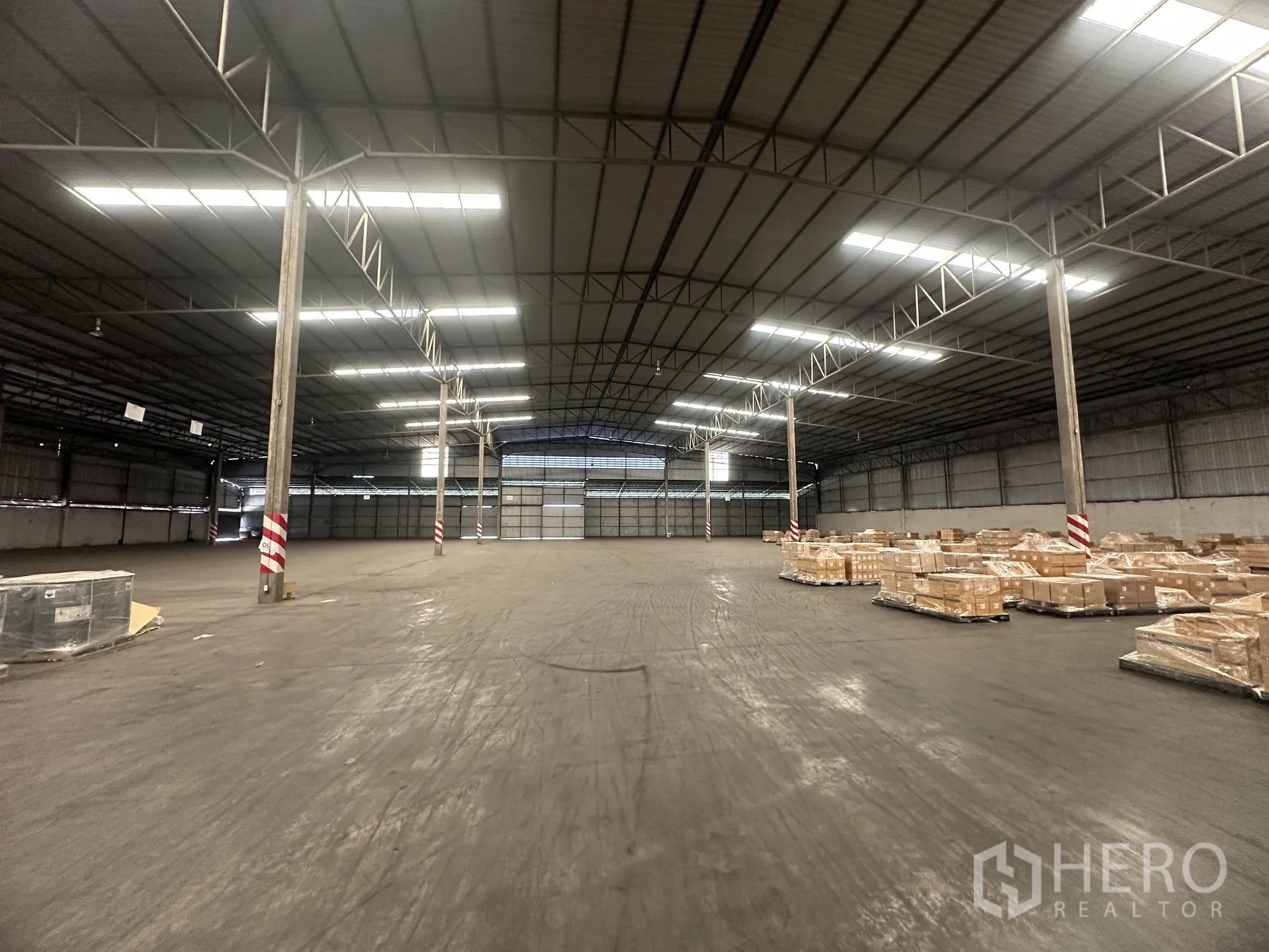 Warehouse for rent in Bang Pa-in, Phra Nakhon Si Ayutthaya - Deep warehouse bay with steel columns, stacked crates on pallets, and rear roller doors.