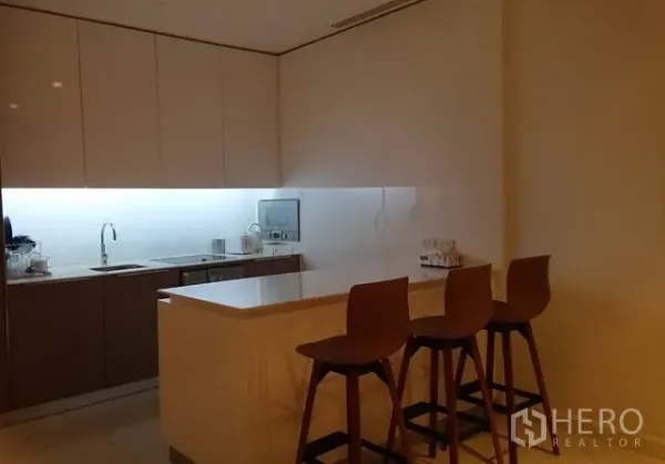公寓 出租在Pathum Wan, Bangkok - 现代厨房设岛台吧台、三把木质高脚椅、简洁柜体与橱柜下照明。