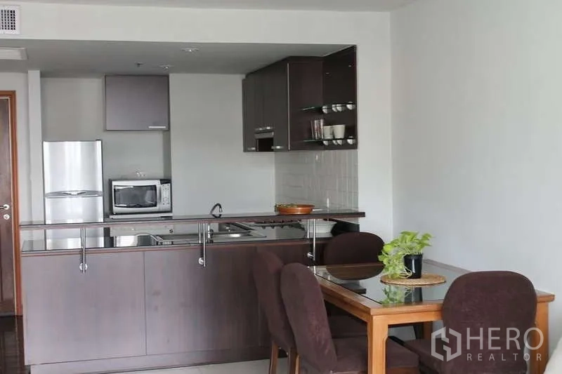 Condominium for rent in Sathon, Bangkok - Dining nook beside the open kitchen with sink, microwave, and refrigerator in a contemporary setup.