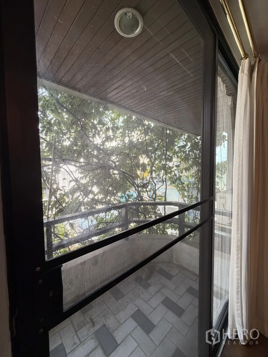 โฮมออฟฟิศ for rent in Watthana, Bangkok - มุมมองสู่ระเบียงเล็กผ่านบานกระจกบานเลื่อนพร้อมมุ้งลวดและพื้นอิฐตัวหนอน