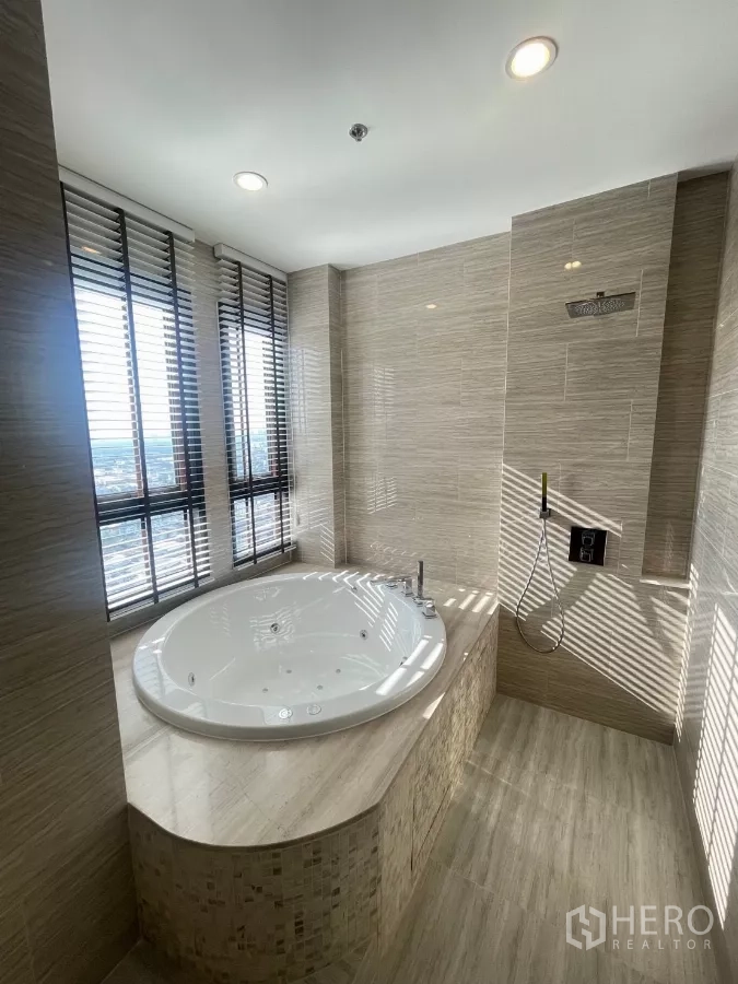 Condominium for rent in Phra Khanong, Bangkok - Spa-style bathroom with round jacuzzi tub by the window and tiled walls.