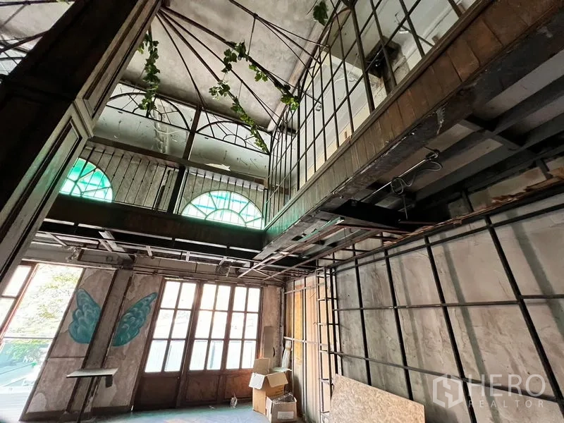 Shophouse for rent in Watthana, Bangkok - Double-height empty room with arched windows, metal mezzanine frame, and vintage wooden doors.
